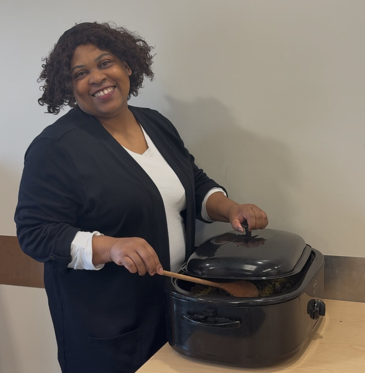 A mid aged black woman stirring a pot of food while smiling